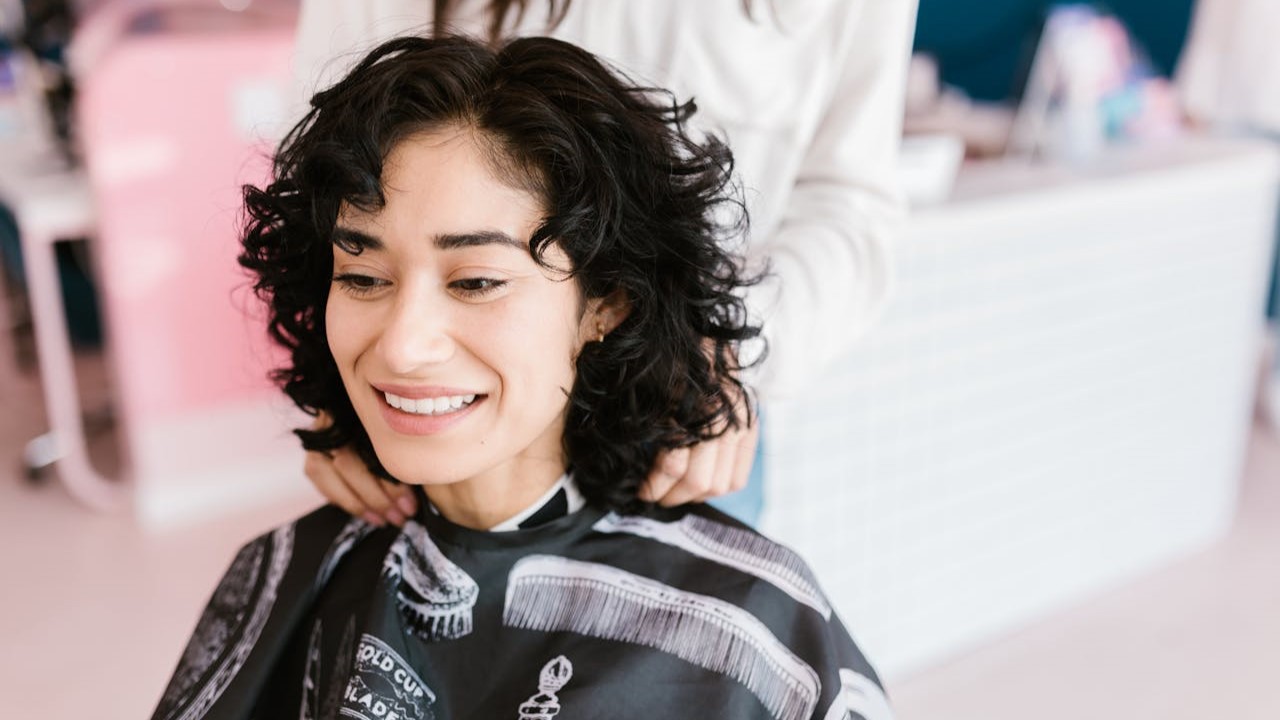 Vrouw met krullend haar glimlacht na het knippen van een moderne wolf cut