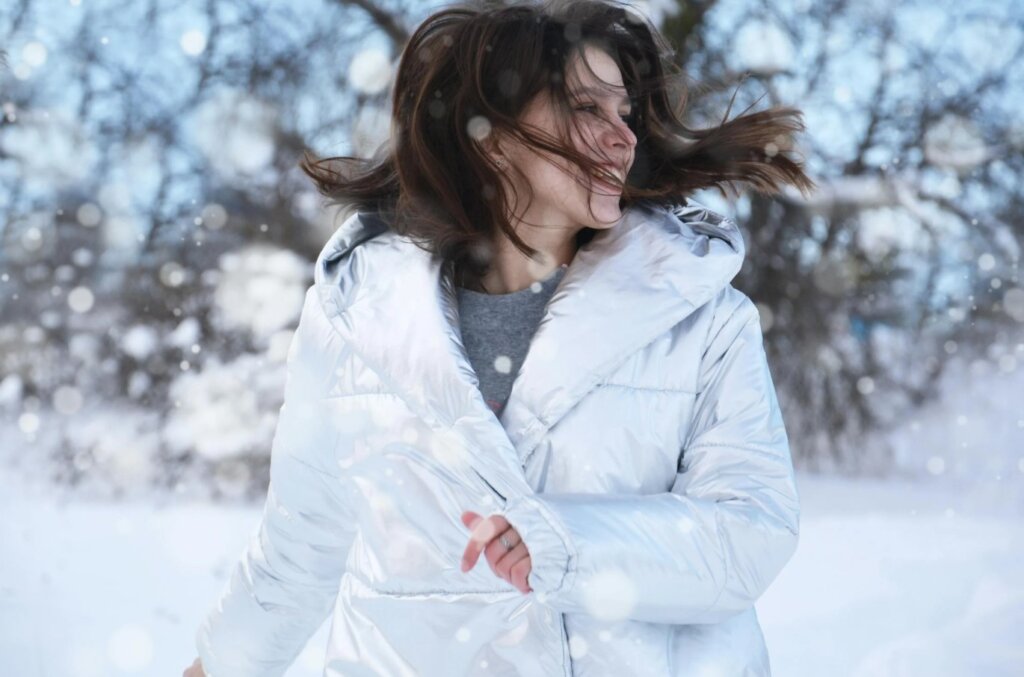 Vrouw in glanzende winterjas geniet van vallende sneeuw op een koude winterdag